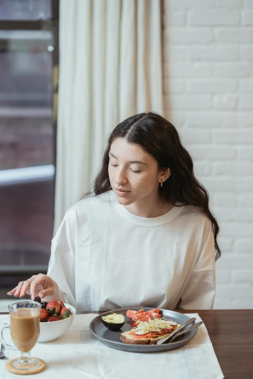 a woman sitting at a table with a plate of food, trending on unsplash, female with long black hair, sydney sweeney, low quality photo, abcdefghijklmnopqrstuvwxyz