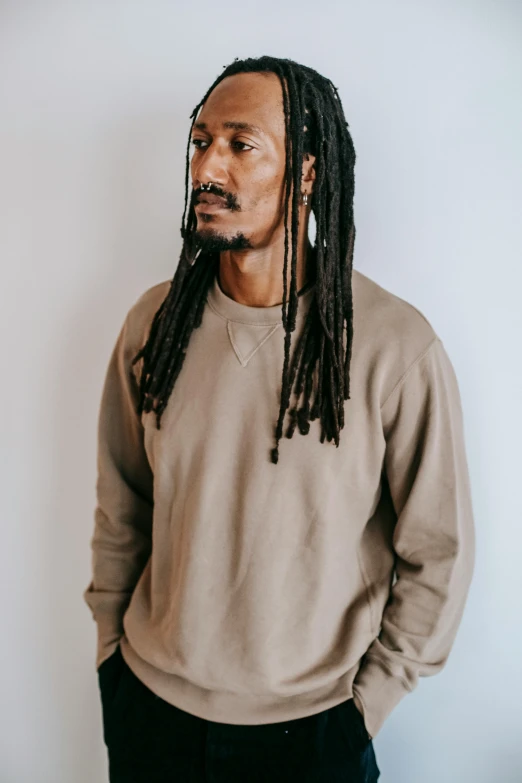 a man with dreadlocks standing in front of a white wall, brown sweater, snoop dog, muted colors. ue 5, thumbnail