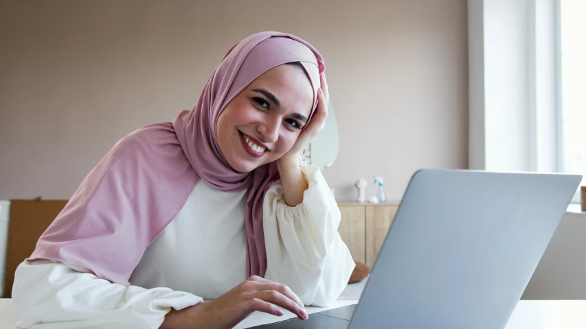 a woman sitting in front of a laptop computer, inspired by Maryam Hashemi, trending on pexels, hurufiyya, with a orientalist smileful face, thumbnail, nursing, lower quality