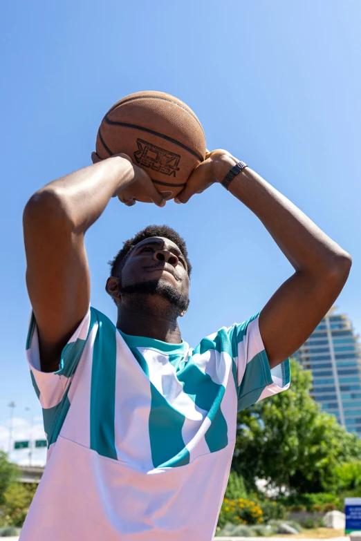 a man holding a basketball over his head, by Washington Allston, trending on unsplash, sea - green and white clothes, looking to the side off camera, summer day, upward shot