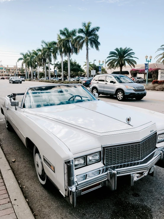 a white cadillac parked on the side of the road, an album cover, by Robbie Trevino, trending on unsplash, renaissance, miami beach, 🎀 🧟 🍓 🧚, convertible, view from the streets