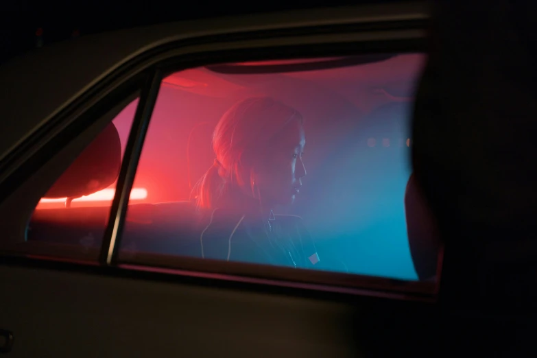 a woman sitting in the passenger seat of a car, inspired by Elsa Bleda, red and blue black light, sad cop looking at a, cinestill 800t 8k, high resolution image