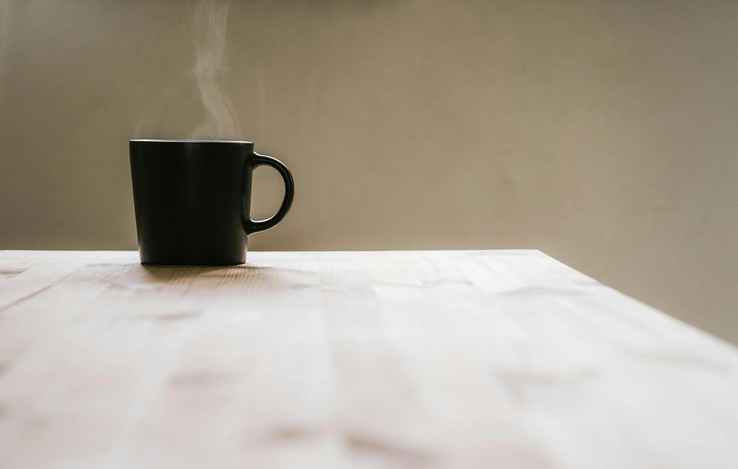 a black coffee cup sitting on top of a wooden table, unsplash, minimalism, foggy, background image, leaked image, soup