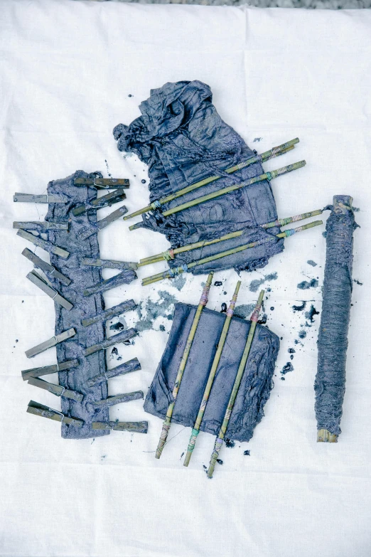 a bunch of sticks sitting on top of a piece of paper, an album cover, inspired by Louise Nevelson, unsplash, assemblage, dark blue segmented armor, tattered fabric, uses explosives, blue and gray colors