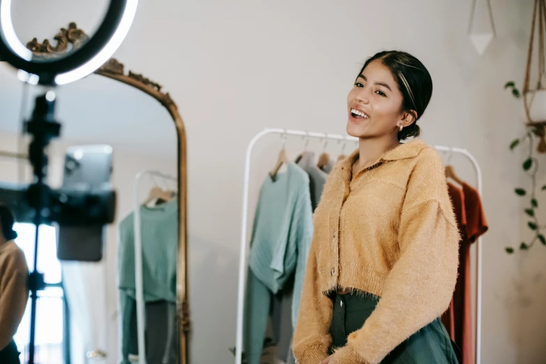 a woman standing in front of a mirror in a room, trending on pexels, hurufiyya, smiling laughing, brown clothes, behind the scenes photo, background image