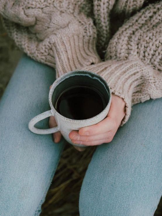 a close up of a person holding a cup of coffee, grey sweater, lynn skordal, cottagecore hippie, low quality photo