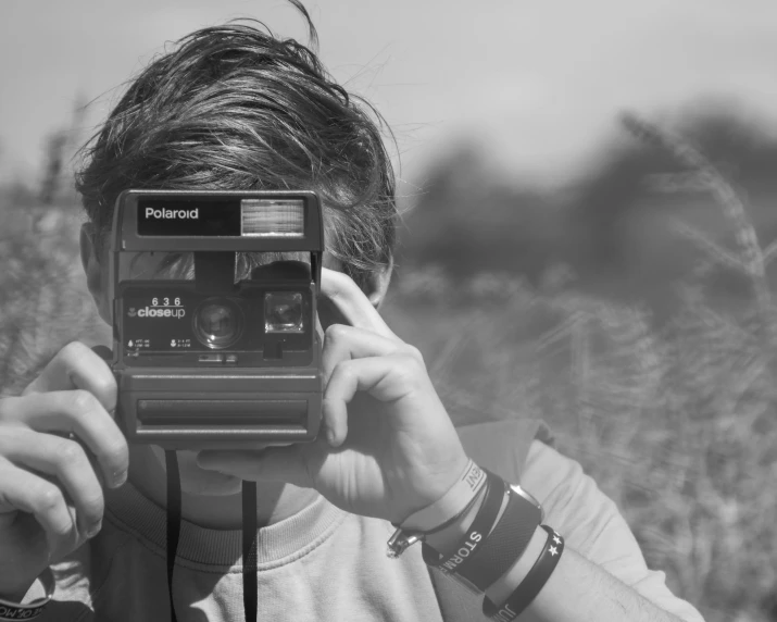 a person taking a picture with a camera, a black and white photo, holding polaroid camera, profile image, field of view, marketing photo