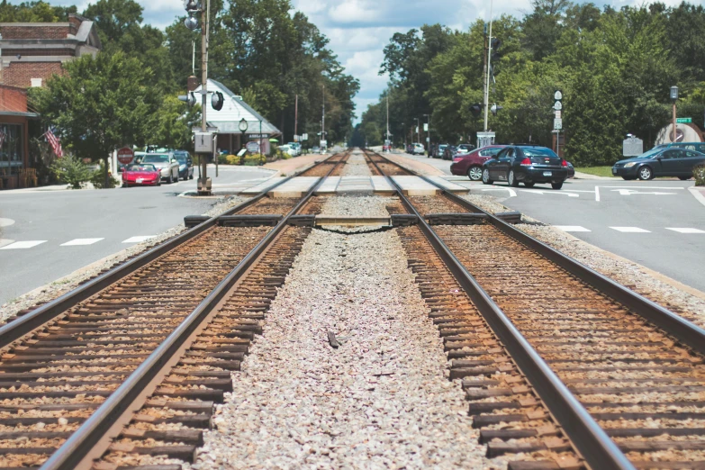 a train traveling down train tracks next to a street, by Carey Morris, unsplash, regionalism, square, trainwreck, summertime, crosswalks