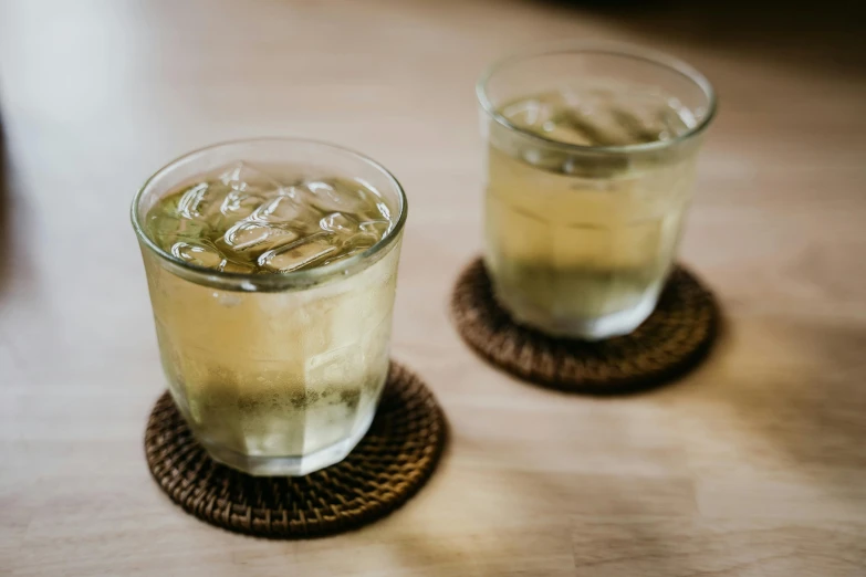 a couple of glasses sitting on top of a wooden table, unsplash, mingei, iced tea glass, green tea, in style of lam manh, taken in the early 2020s