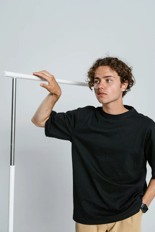 a man wearing a black t - shirt and khaki pants, an album cover, by Jacob Toorenvliet, dancing on a pole, iv pole, looking off to the side, in front of white back drop