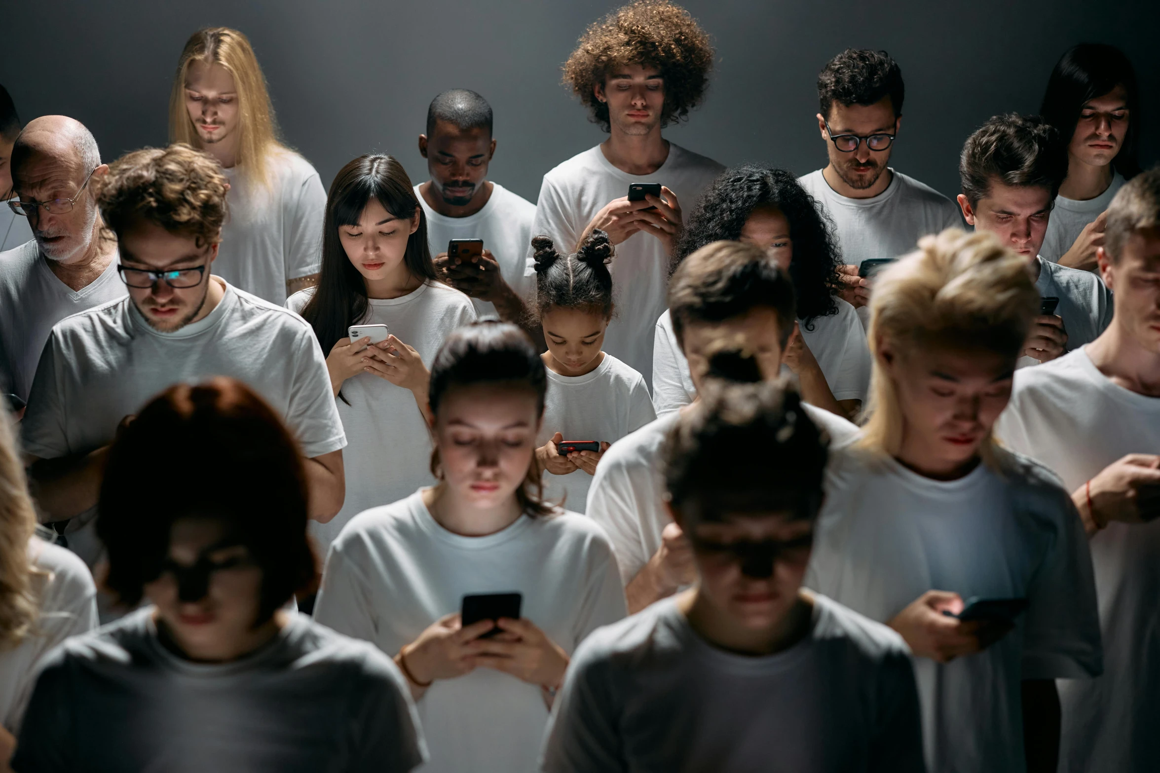 a group of people looking at their cell phones, trending on pexels, antipodeans, dressed in a white t shirt, avatar image, dark, in rows