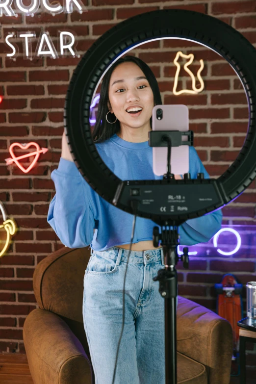 a woman that is standing in front of a camera, a hologram, by Robbie Trevino, trending on pexels, ring light, joy ang, teenager hangout spot, product introduction photo