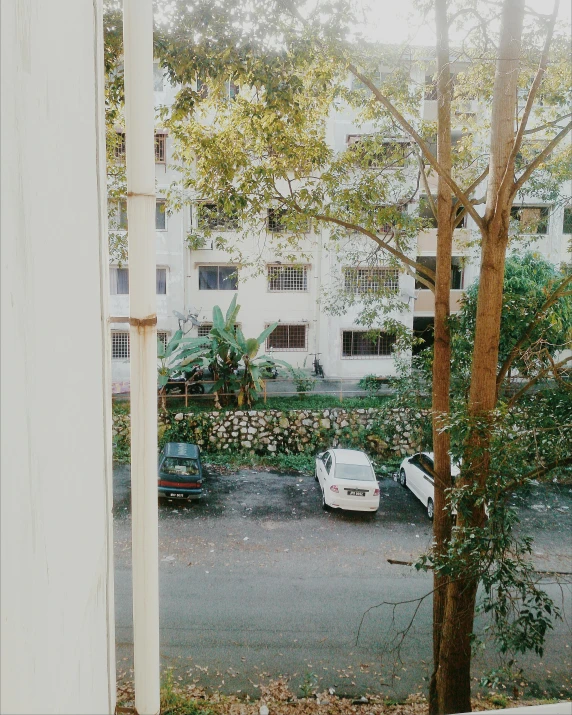 a view of a parking lot from a window, a polaroid photo, inspired by Elsa Bleda, unsplash, assamese aesthetic, trees!!, balcony, white building