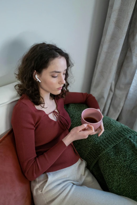 a woman sitting on a couch holding a cup of coffee, inspired by Louisa Matthíasdóttir, happening, earbuds, drinking cough syrup, pink, close up photograph