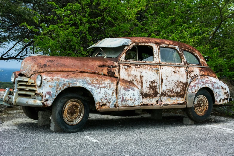 an old rusty car parked in a parking lot, by Robert Storm Petersen, pexels contest winner, auto-destructive art, 1 9 3 7 pontiac sedan, made of tar, upon a peak in darien, preserved historical