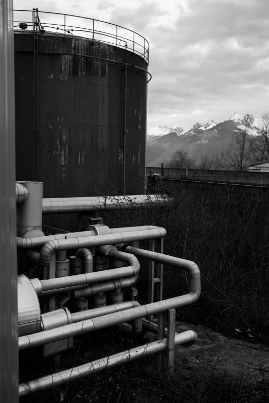 a black and white photo of pipes and tanks, a black and white photo, inspired by Siegfried Haas, flickr, the alps are in the background, vibrant but dreary, ((rust)), lab in the background