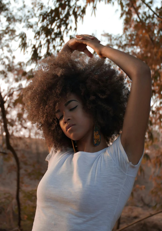 a woman standing under a tree with her hands on her head, pexels contest winner, renaissance, big afro, curly bangs and ponytail, early morning lighting, black young woman