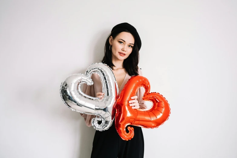 a woman in a black dress holding two red and silver balloons, pexels contest winner, holding a 🛡 and an 🪓, hearts, product introduction photo, background image