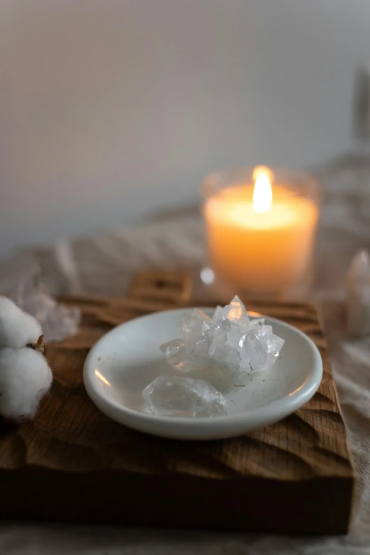 a white plate sitting on top of a wooden cutting board, inspired by Kim Tschang Yeul, crystals enlight the scene, candle, close up of single sugar crystal, bubble bath