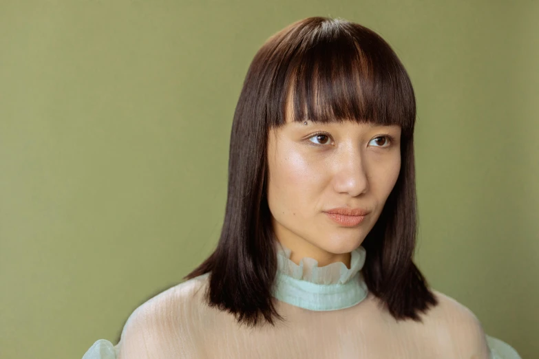 a woman standing in front of a green wall, an album cover, inspired by Yukimasa Ida, trending on pexels, mingei, with dark brown bangs, closeup headshot portrait, square jaw-line, ethnicity : japanese