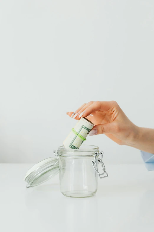 a person putting money in a jar on a table, a stock photo, by Byron Galvez, minimalism, 🐿🍸🍋, on a white background, banana, 15081959 21121991 01012000 4k