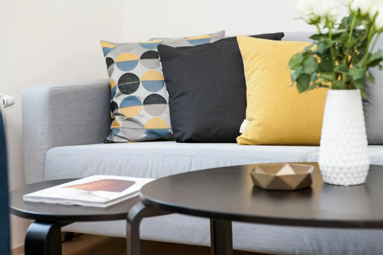 a couch sitting in a living room next to a table, inspired by Bauhaus, trending on unsplash, some sandy yellow pillows, medium closeup, light grey blue and golden, charcoal and silver color scheme