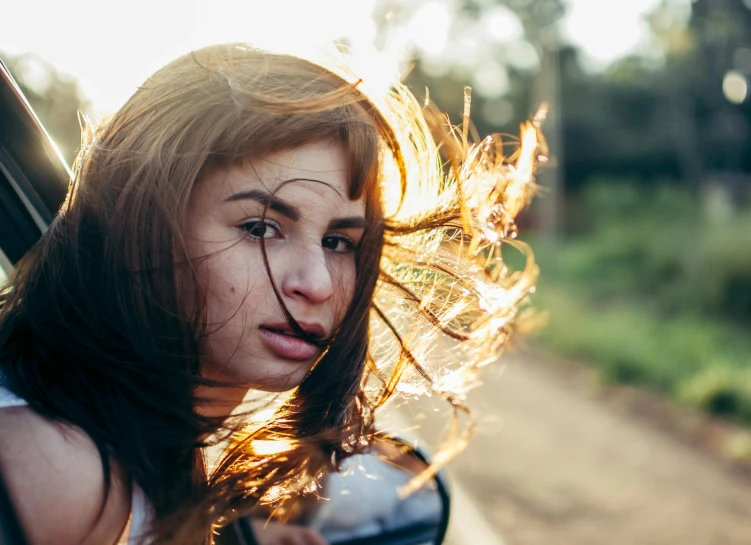 a woman looking out the window of a car, trending on pexels, her hair blowing in the wind, golden light, portrait of teen girl, swirling around