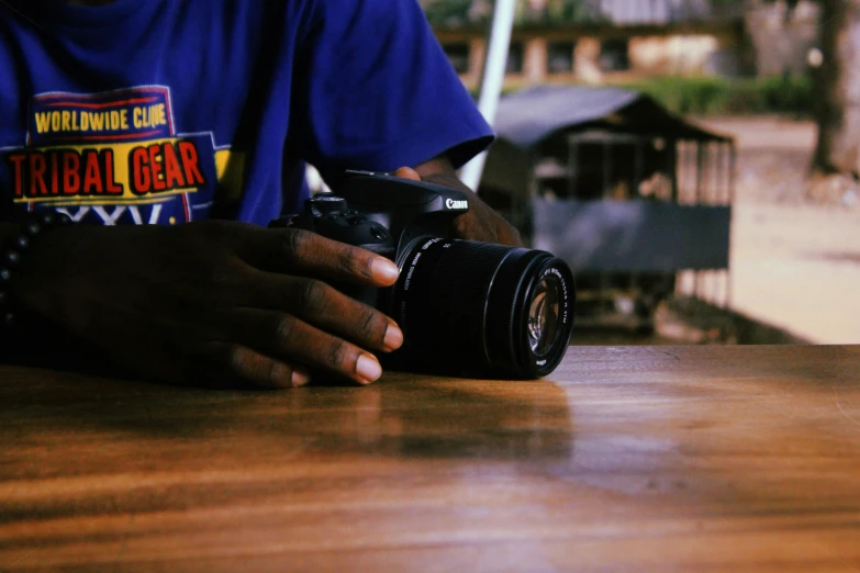 a man sitting at a table holding a camera, a picture, on a wooden table, photography: journalism, uploaded, canon shot