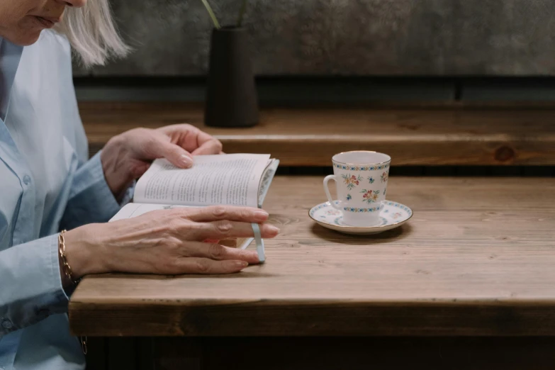 a woman sitting at a table reading a book, by Matija Jama, trending on unsplash, the sacred cup of understading, old testament, a wooden, praying