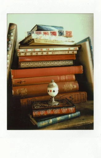 a stack of books sitting on top of a wooden table, a still life, by Aileen Eagleton, renaissance, polaroide photo, ( ( photograph ) ), postcard, antiques
