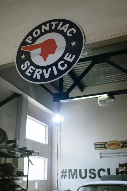 a car parked inside of a garage next to a sign, by Robert Peak, private press, hanging from the ceiling, with an eagle emblem, maintenance area, polaeized light