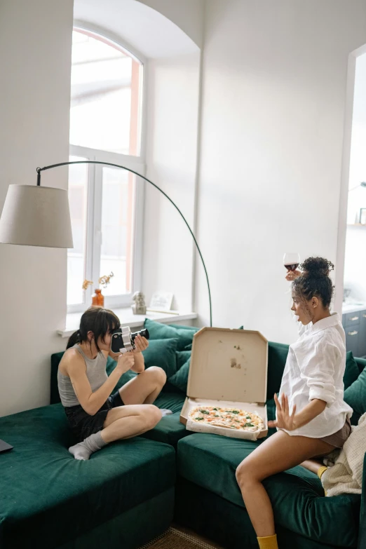 a couple of women sitting on top of a green couch, a photo, inspired by Elsa Bleda, trending on pexels, cooking pizza, in suitcase, on a white table, taking a picture