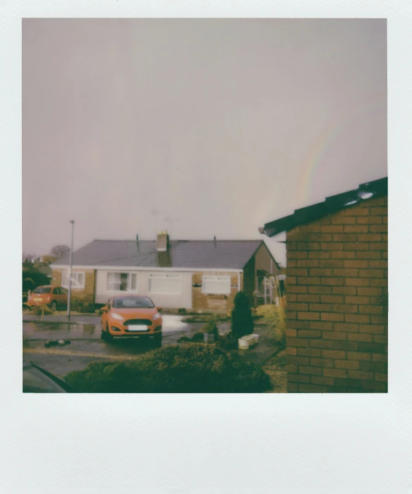 a car is parked in front of a house, a polaroid photo, by IAN SPRIGGS, unsplash, postminimalism, grey skies with two rainbows, faded red and yelow, roofs, clear skies in the distance