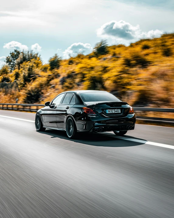 a car driving down a highway with trees in the background, by Sebastian Spreng, pexels contest winner, purism, mercedez benz, profile image, black rims, back turned