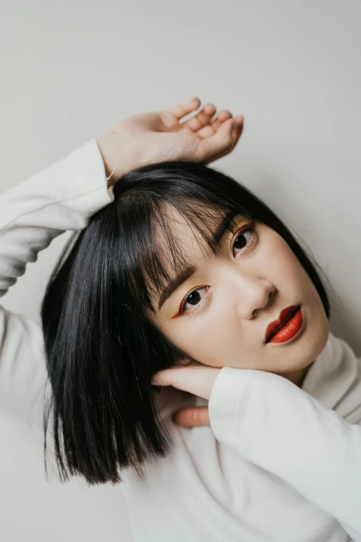 a woman leaning against a wall with her hands on her head, an album cover, inspired by Ma Yuanyu, trending on pexels, hair blackbangs hair, closeup headshot portrait, lipstick, asian human