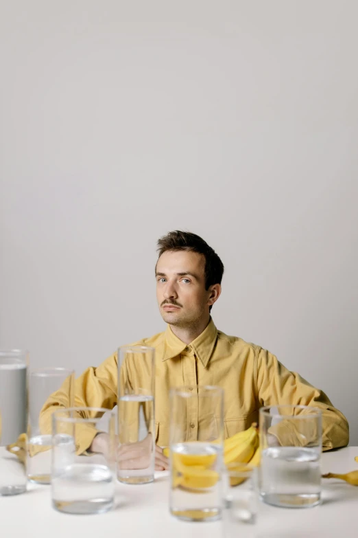 a man sitting at a table with a banana in front of him, an album cover, by Leo Leuppi, thin moustache, flume, high quality photo, calm face