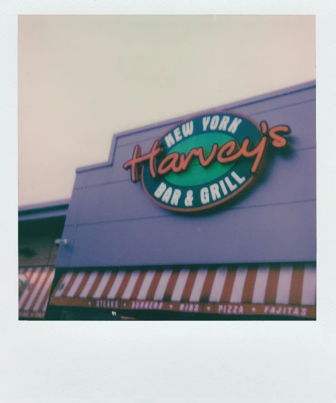 a sign on the side of a building that says harvey's bar and grill, a polaroid photo, unsplash, hi-res scan, alternate album cover, hazy, medium format