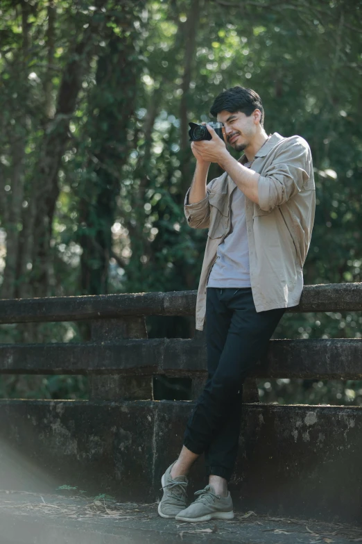 a man sitting on a fence taking a picture, inspired by Adam Dario Keel, pexels contest winner, realism, in a jungle environment, asian male, walking, brown