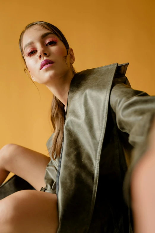 a beautiful young woman sitting on top of a bed, trending on pexels, photorealism, leather trench coat, aggressive pose, upclose, at a fashion shoot