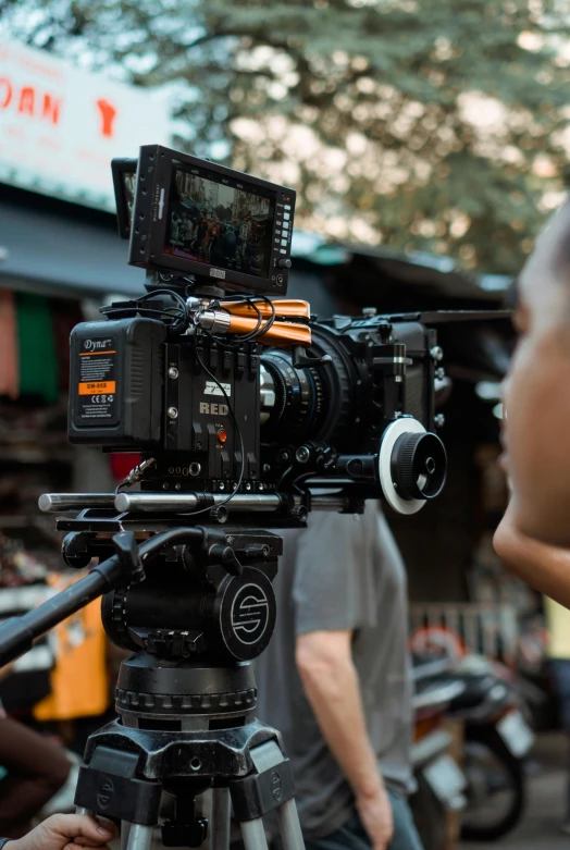 a man standing next to a camera on a tripod, arri alfa anamorphic lens, cctv footage of a movie set, shot on alexa, close up camera angle