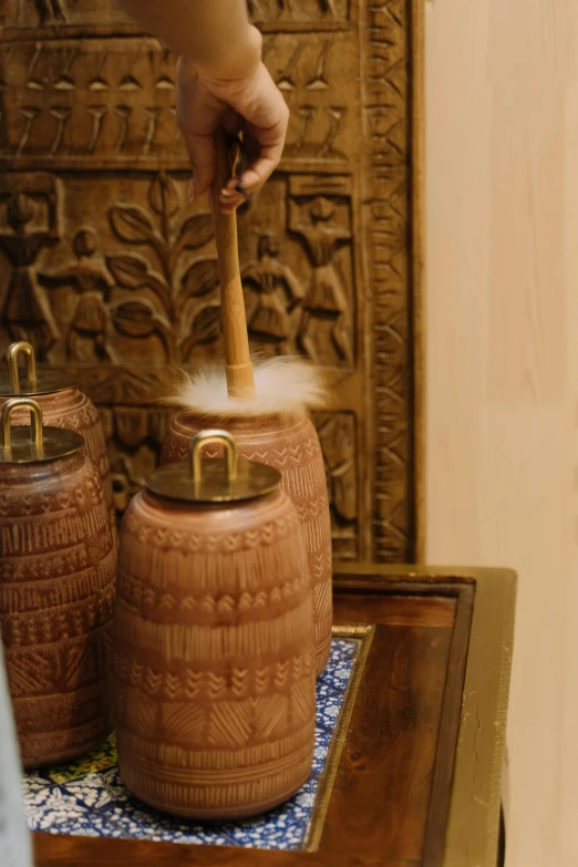 a close up of a person putting something in a jar, inspired by Riad Beyrouti, hurufiyya, drums, spa, with detailed wood, pure gold pillars