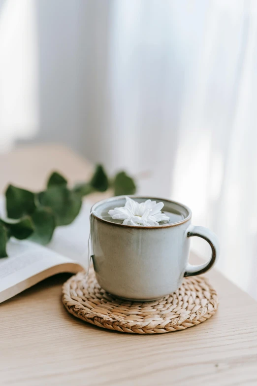 a cup of coffee sitting on top of a wooden table, by Tan Ting-pho, hurufiyya, white petal, cozy environment, grey, detailed product image