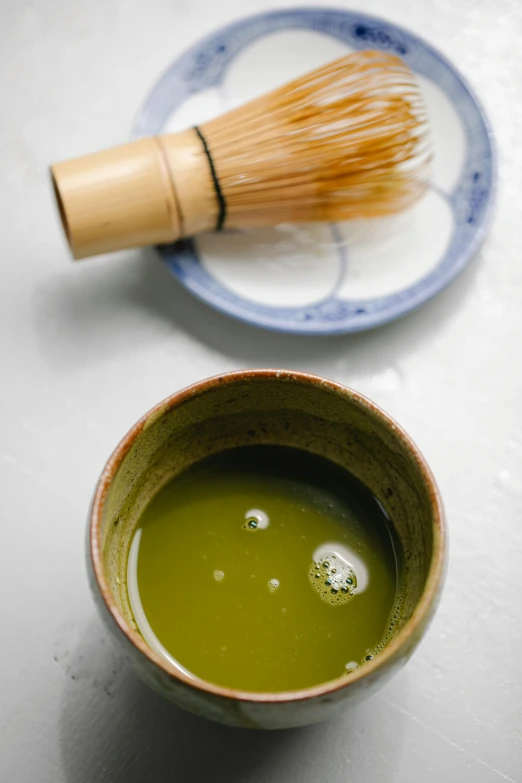 a bowl of green tea next to a whisk, inspired by Kanō Shōsenin, square, beautiful green liquid, made of glazed, abcdefghijklmnopqrstuvwxyz