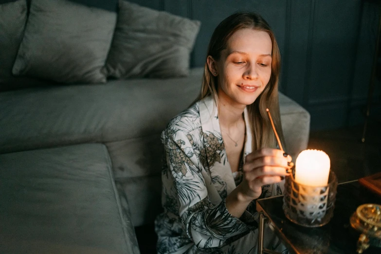 a woman sitting on a couch holding a lit candle, trending on pexels, warm smile, gas lighting, sitting on a bed, fine intricate