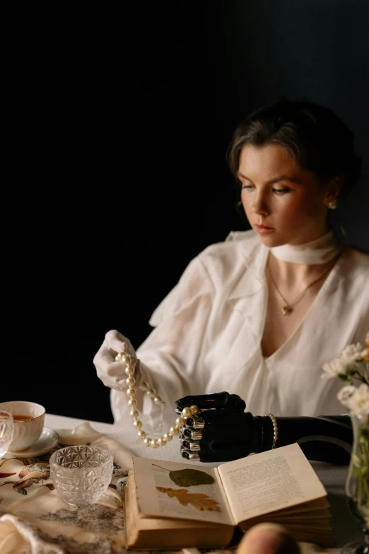 a woman sitting at a table reading a book, a portrait, inspired by Cecil Beaton, unsplash, white long gloves, fashion shoot 8k, pearl necklace, anna nikonova aka newmilky