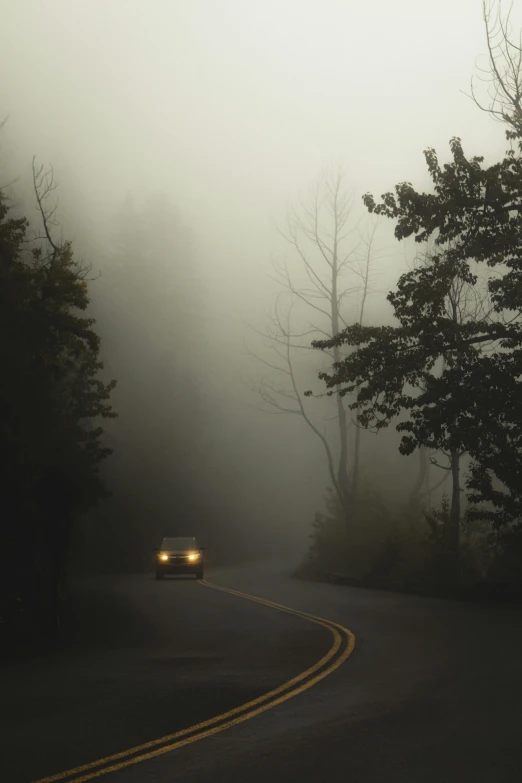 a car is driving down a foggy road, inspired by Elsa Bleda, tonalism, ominous! landscape of north bend, eerie ”