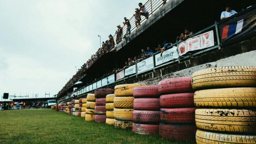 a row of tires sitting on top of a grass covered field, unsplash, process art, crowded stands, villeneuve, guardrails, vintage colours