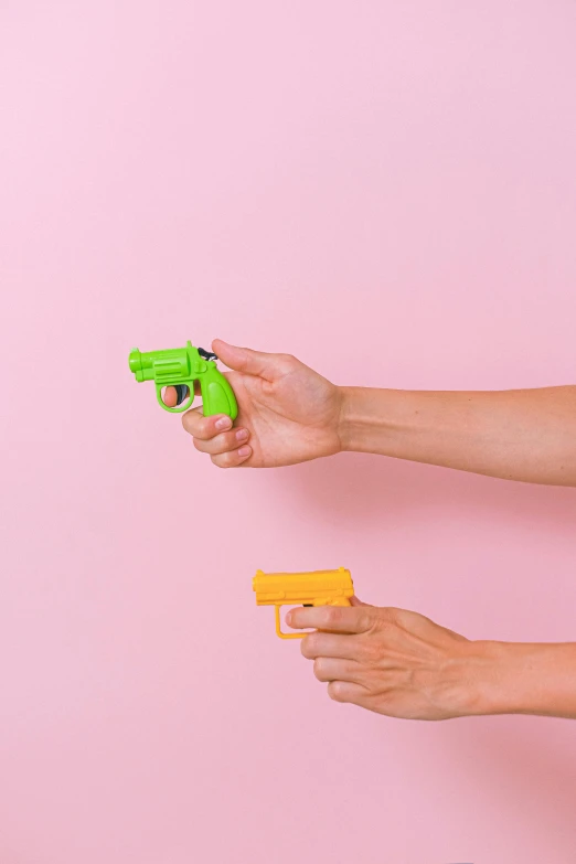 two women are playing with toy guns against a pink background, by Carey Morris, pexels, conceptual art, single pair of hands, green arms, instagram post, background image