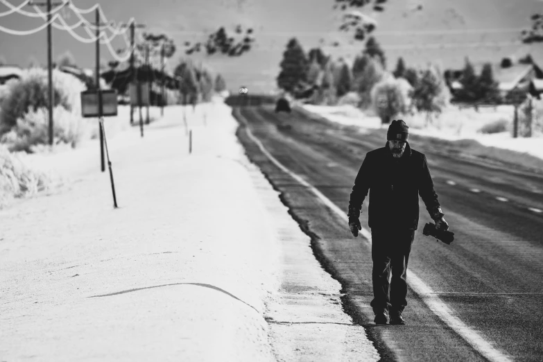 a man walking down a snow covered road, a black and white photo, by Mike Bierek, unsplash, walter white from breaking bad, background image, musician, broken down