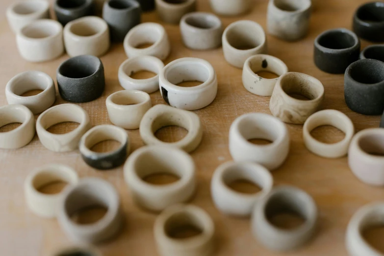 a bunch of rings sitting on top of a wooden table, a marble sculpture, by Helen Stevenson, trending on unsplash, mingei, made of clay, bone and ivory, holes, in a row